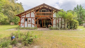 A traditional wooden house with a balcony, surrounded by a grassy yard and trees.