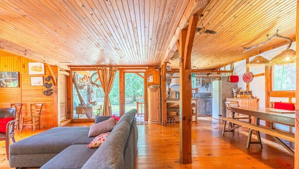 A wooden cabin interior with a sofa, dining table, and kitchen area.