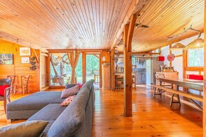 Interior de una cabaña de madera con sofá, mesa de comedor y zona de cocina.