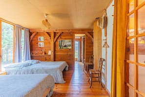 Una cabaña de madera con dos camas, una zona de comedor y un amplio ventanal.