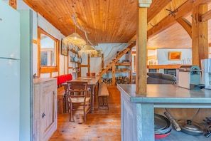 Una cocina rústica con vigas de madera, una zona de comedor con bancos y una escalera que sube a otro nivel.