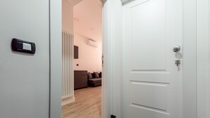 A modern hotel room with a wooden floor, a white door, and a view into the living area with a sofa and a radiator. - Via Niccol Tommaseo 4 - Appartamento 5 (Naples)
