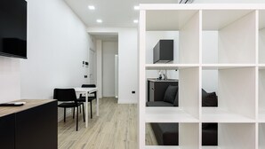 A modern, well-lit room with a flat-screen TV, a dining area with a table and chairs, and a built-in shelving unit with a microwave and seating. - Via Niccol Tommaseo 4 - Appartamento 5 (Naples)