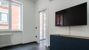 A modern room with a large window, a radiator, a dark blue cabinet, and a mounted flat-screen TV. - Via Niccol Tommaseo 4 - Appartamento 6 (Naples)