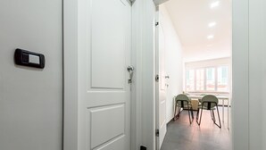 A hallway with white doors, a dining area with four chairs, and a view of the outside through large windows. - Via Niccol Tommaseo 4 - Appartamento 6 (Naples)