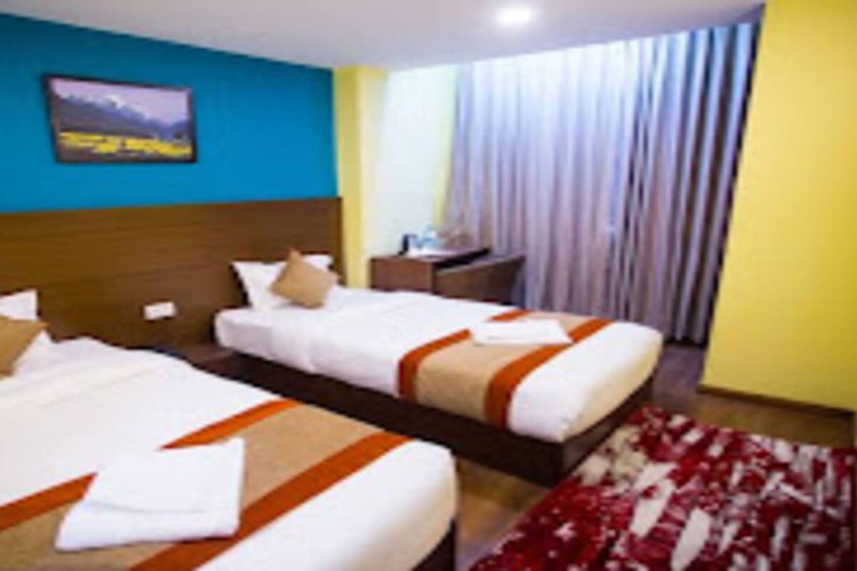 A hotel room with two beds, a wooden headboard, a painting on the wall, a desk, and a window with curtains.
