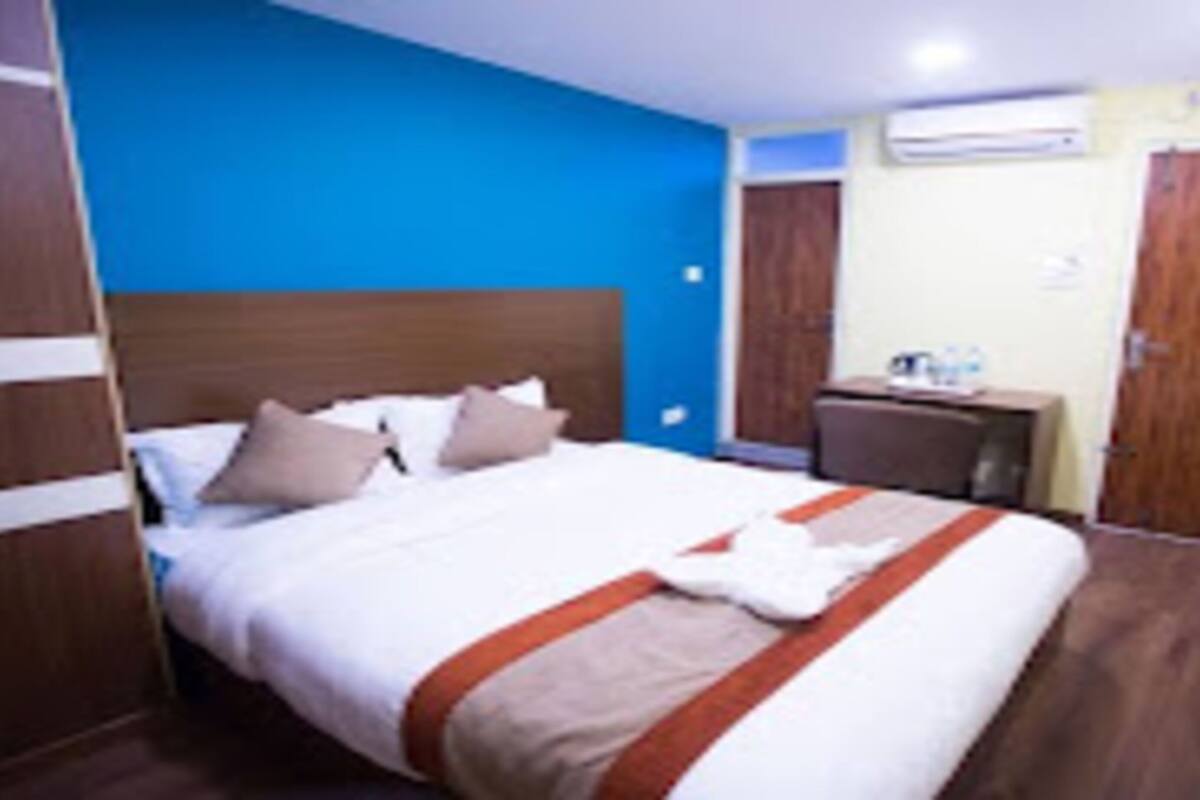 A hotel room with a large bed, a wooden headboard, a desk with a chair, and a wardrobe.