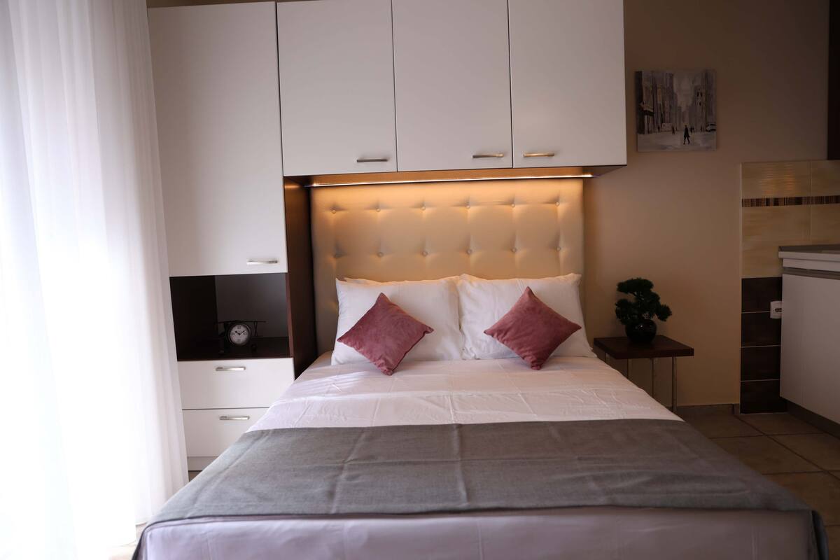 Une chambre d’hôtel avec un grand lit, une table de chevet avec une horloge, une petite plante en pot et un tableau au mur.