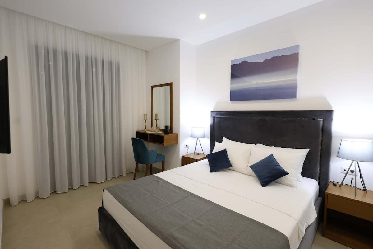 Une chambre d’hôtel avec un grand lit, un bureau avec une chaise, une table de chevet avec une lampe et un tableau au mur.