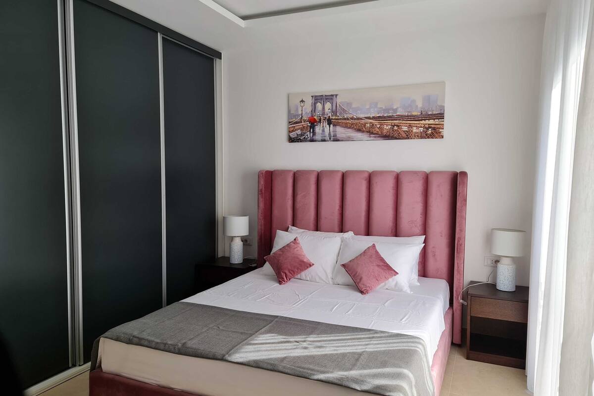 Une chambre d’hôtel avec un grand lit, une tête de lit, deux tables de chevet et un tableau au mur.