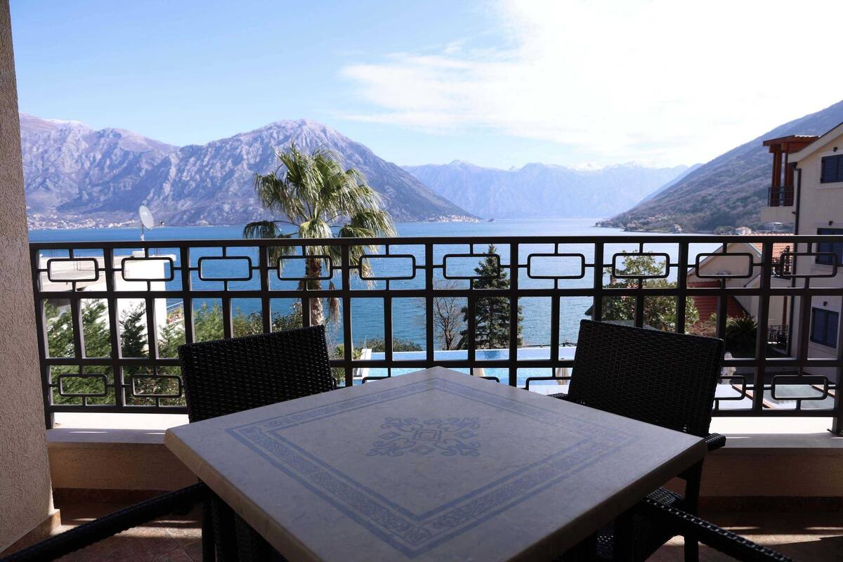 Un balcon avec une table et des chaises, donnant sur un lac et des montagnes.