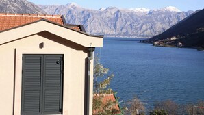 A building with a beige facade and dark shutters, overlooking a calm lake with mountains in the background. - Bellezza Resort & SPA (Morinj)