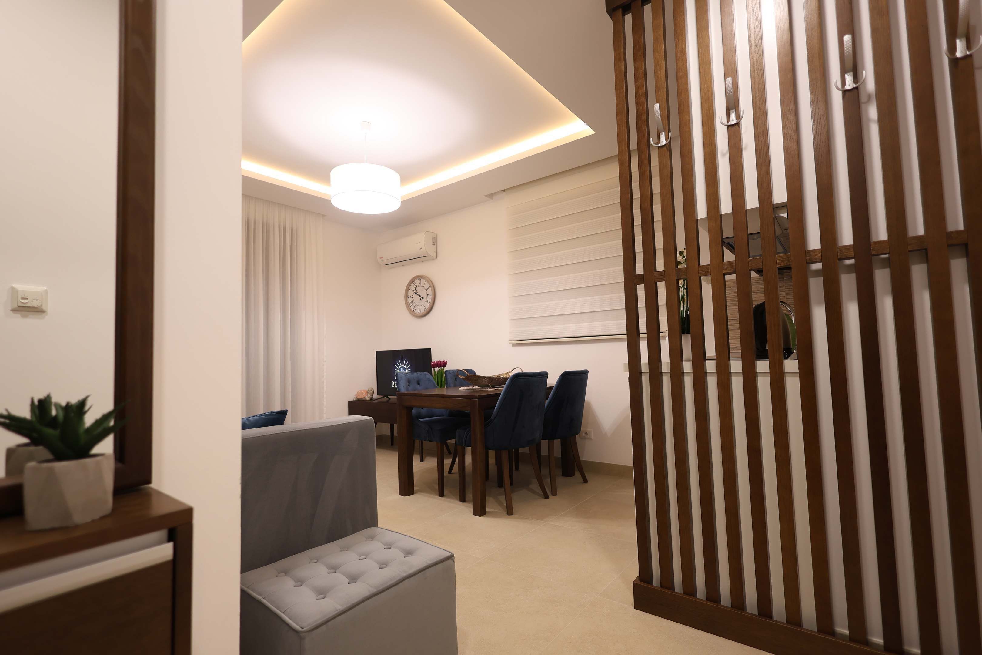 A modern living room with a dining area, a grey sofa, a wooden sideboard, and a decorative plant.