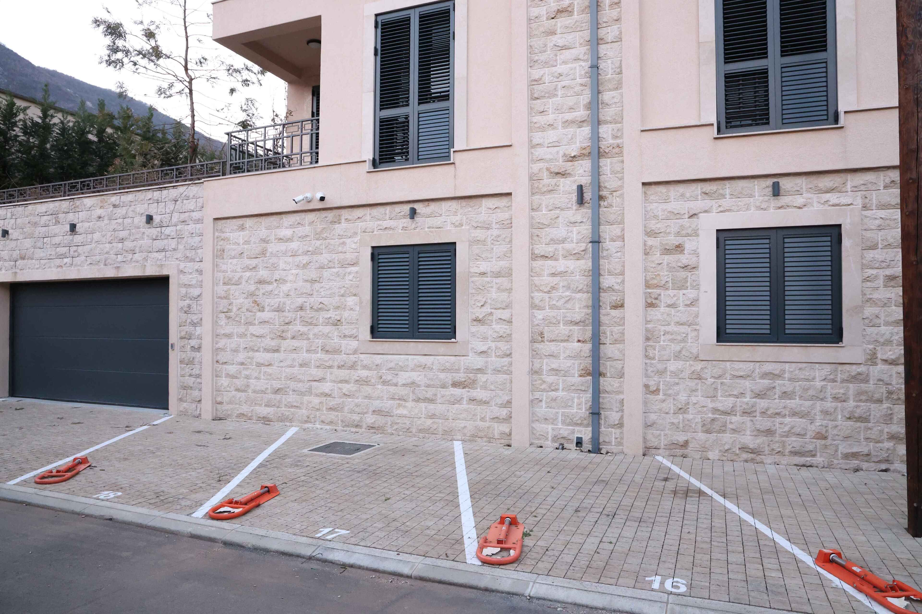 Un espace de stationnement avec des places délimitées, une porte de garage et un bâtiment à la façade en pierre et aux volets.