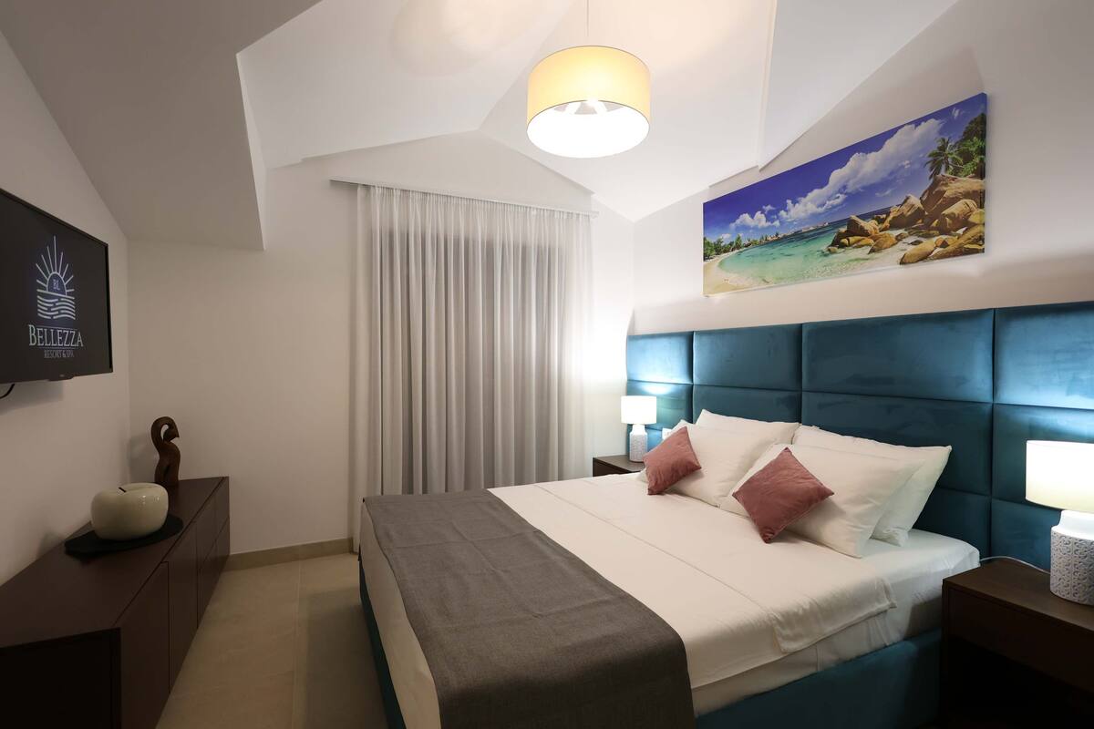 Une chambre d’hôtel avec un grand lit, une tête de lit ornée d’un tableau, un téléviseur à écran plat et une table de chevet avec une lampe.