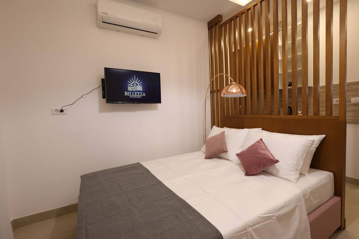 Une chambre d’hôtel avec un lit, un téléviseur fixé au mur et une cloison en bois.