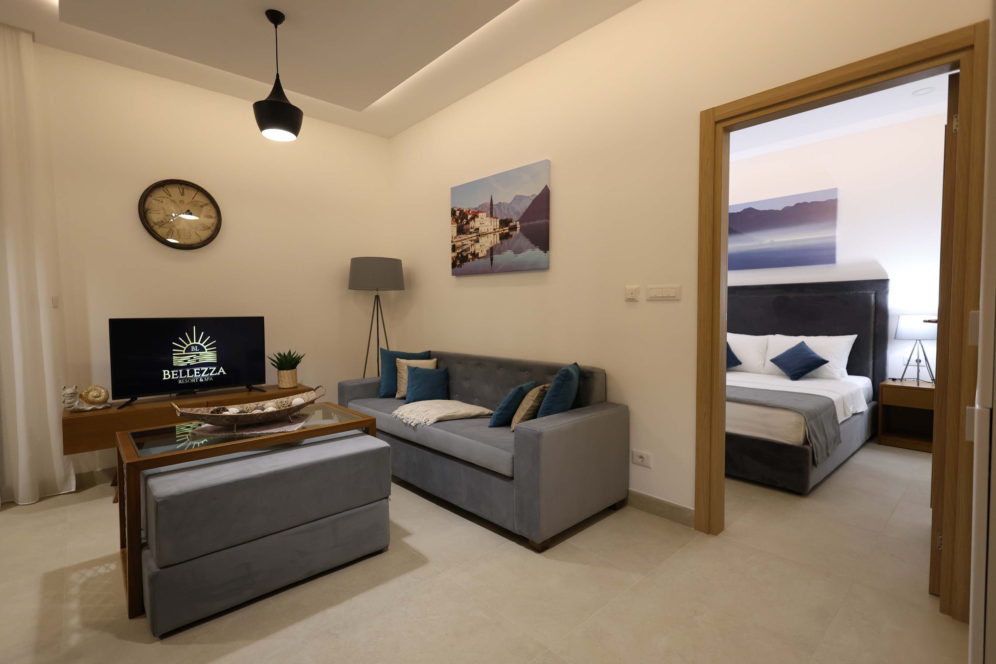 Een moderne woonkamer met een grijze bank, een salontafel, een televisie en een schilderij aan de muur.