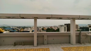 Une terrasse sur le toit, ornée de carreaux jaunes et blancs formant un motif, avec une rambarde en métal et une vue sur le paysage urbain en arrière-plan.