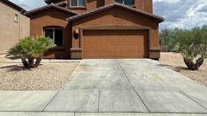 A two-story house with a garage, a driveway, and two palm trees.