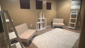 A room with a white sofa, a white rug, a ladder, and a small table with decorative items.