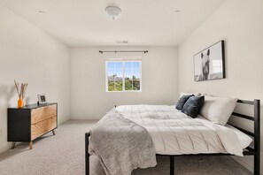 A bedroom with a bed, a window, a picture on the wall, and a dresser.