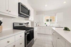 Una cucina moderna con mobili bianchi, forno integrato, microonde e cappa aspirante in acciaio inox.