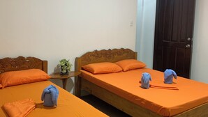 Twee houten bedden met oranje beddengoed, een kleine tafel met een plant, en een donkere deur.