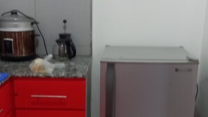 Een compacte keuken met een rode kast, een roestvrijstalen koelkast en een klein aanrecht met een waterkoker.
