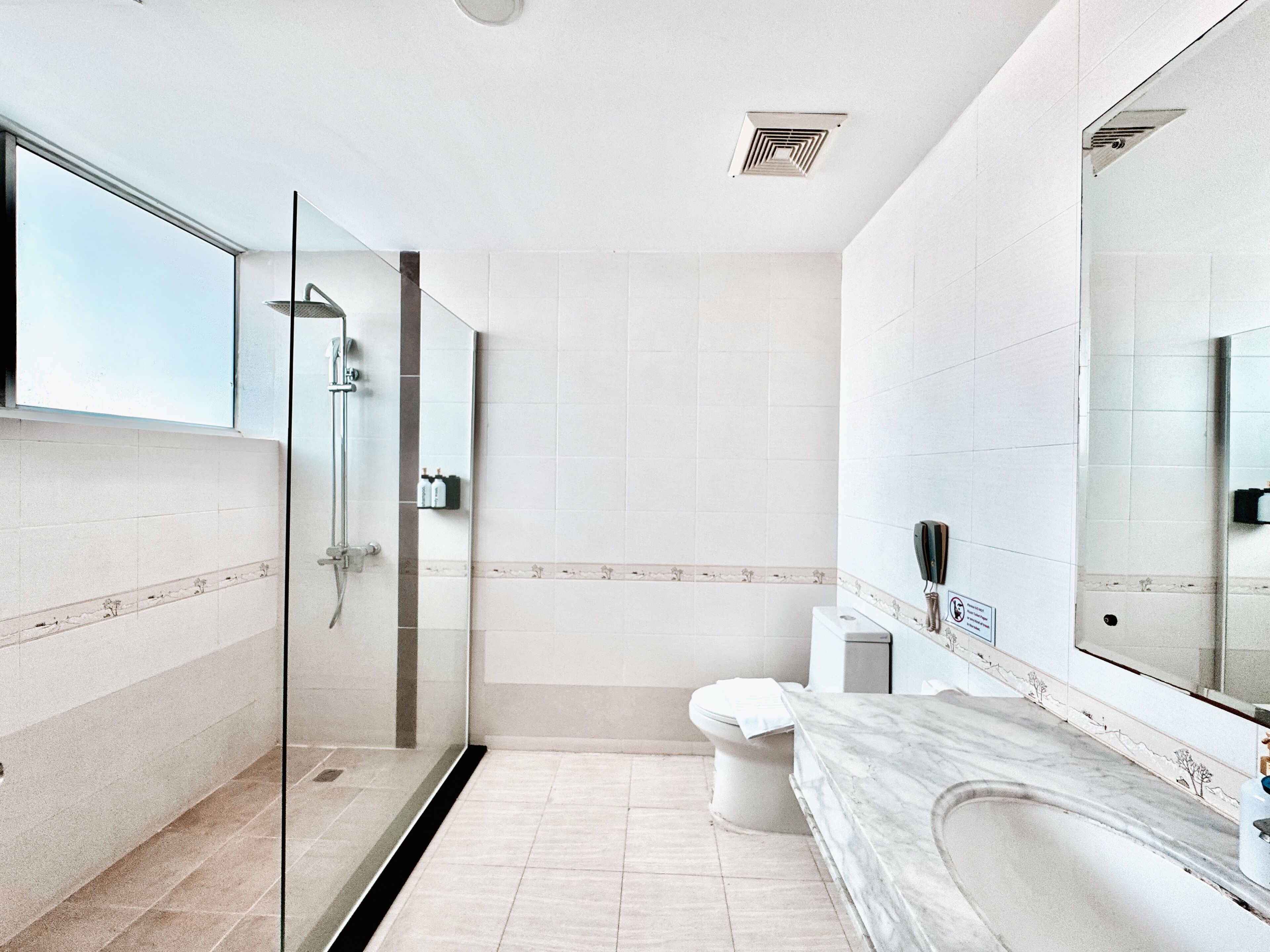 Een moderne badkamer met een douchecabine van glas, een marmeren wastafel en een grote spiegel.