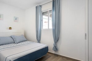 Une chambre à coucher avec un lit, des rideaux, une fenêtre, une étagère fixée au mur avec une plante et une tête de lit.