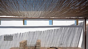 Ein überdachter Sitzbereich im Freien mit Grill, Holzblöcken und einem Metallgestell.