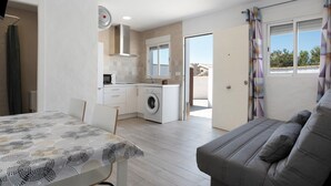 Eine moderne Wohnung mit Essbereich, einer Couch, einer Küche inklusive Waschmaschine und einer Schiebetür zu einem Außenbereich.