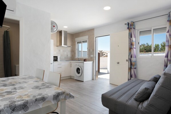 Un appartement moderne comprenant un coin repas, un canapé, une cuisine avec machine à laver et une porte coulissante donnant sur un espace extérieur.