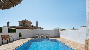 A swimming pool with a stone border, a bench, and lounge chairs.