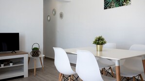 A modern dining area with a white table, white chairs, a television on a wooden stand, and a small plant on the table.