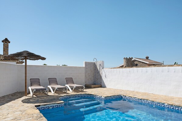 A swimming pool with lounge chairs, a brick wall, and a stone tower. - Vacation Home "Casa Luype 2" with 2 Private Terraces, Shared Pool & Wi-Fi (Conil)