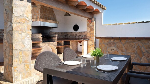 An outdoor dining area with stone walls, a brick oven, and a table set for two.