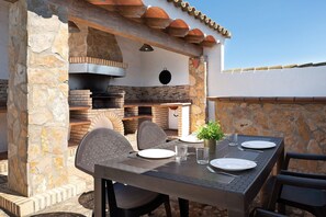 An outdoor dining area with stone walls, a brick oven, and a table set for two. - Vacation Home "Casa Luype 2" with 2 Private Terraces, Shared Pool & Wi-Fi (Conil)