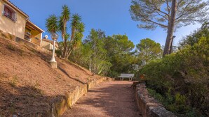 A pathway leading to a bench, surrounded by trees and a building with a balcony. - Villa 'Rez De Jardin Dans' with Private Pool, Private Terrace and Wi-Fi (Saint-Raphaël)