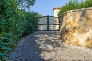 A stone pathway leading to a gated entrance with a stone wall on one side and a hedge on the other. - Villa 'Rez De Jardin Dans' with Private Pool, Private Terrace and Wi-Fi (Saint-Raphaël)