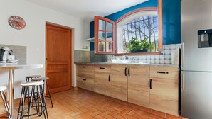A kitchen with wooden cabinets, a stainless steel refrigerator, a window with a view, and a clock on the wall. - Villa 'Rez De Jardin Dans' with Private Pool, Private Terrace and Wi-Fi (Saint-Raphaël)
