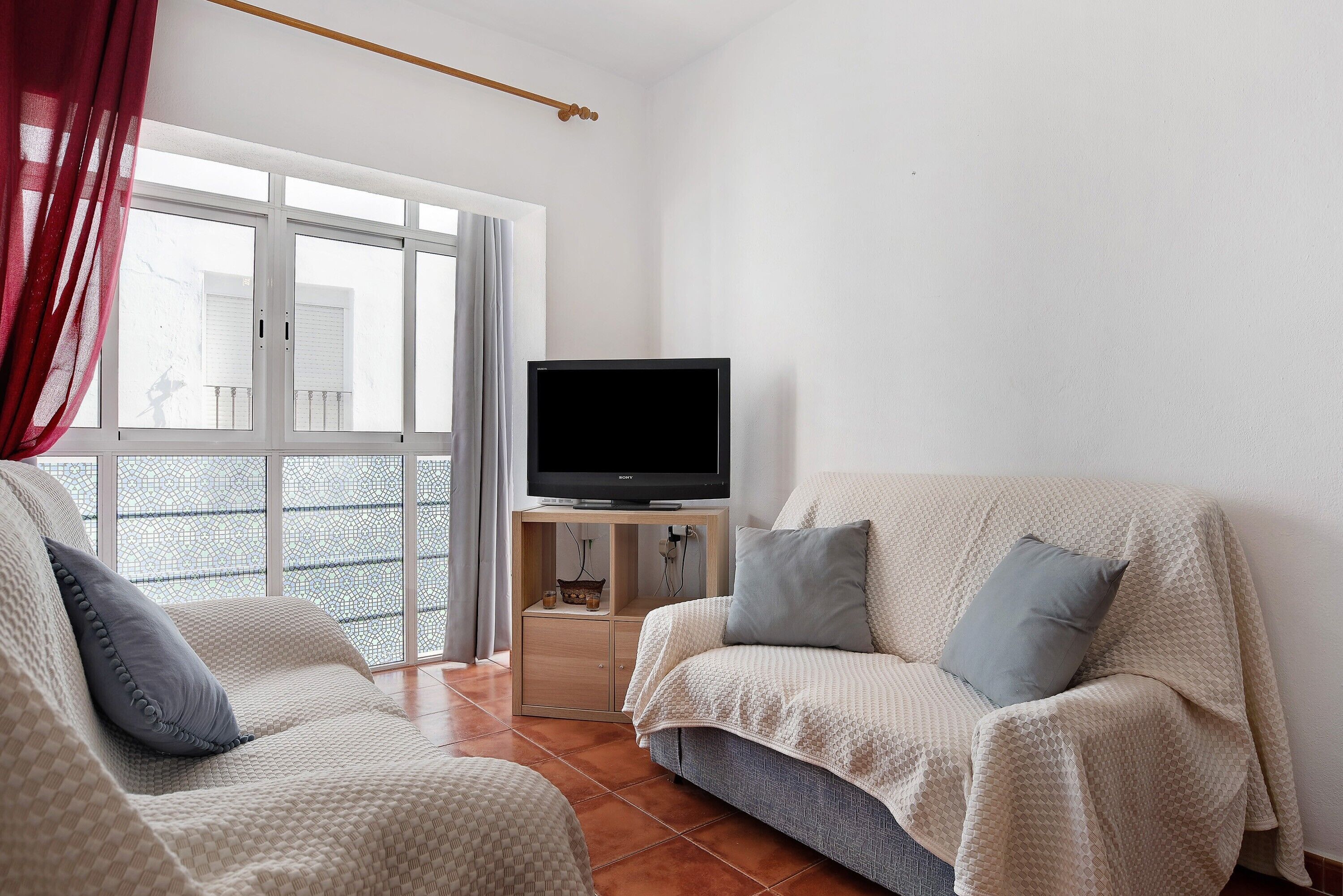 A living room with a sofa, a television on a stand, and a view through a window.
