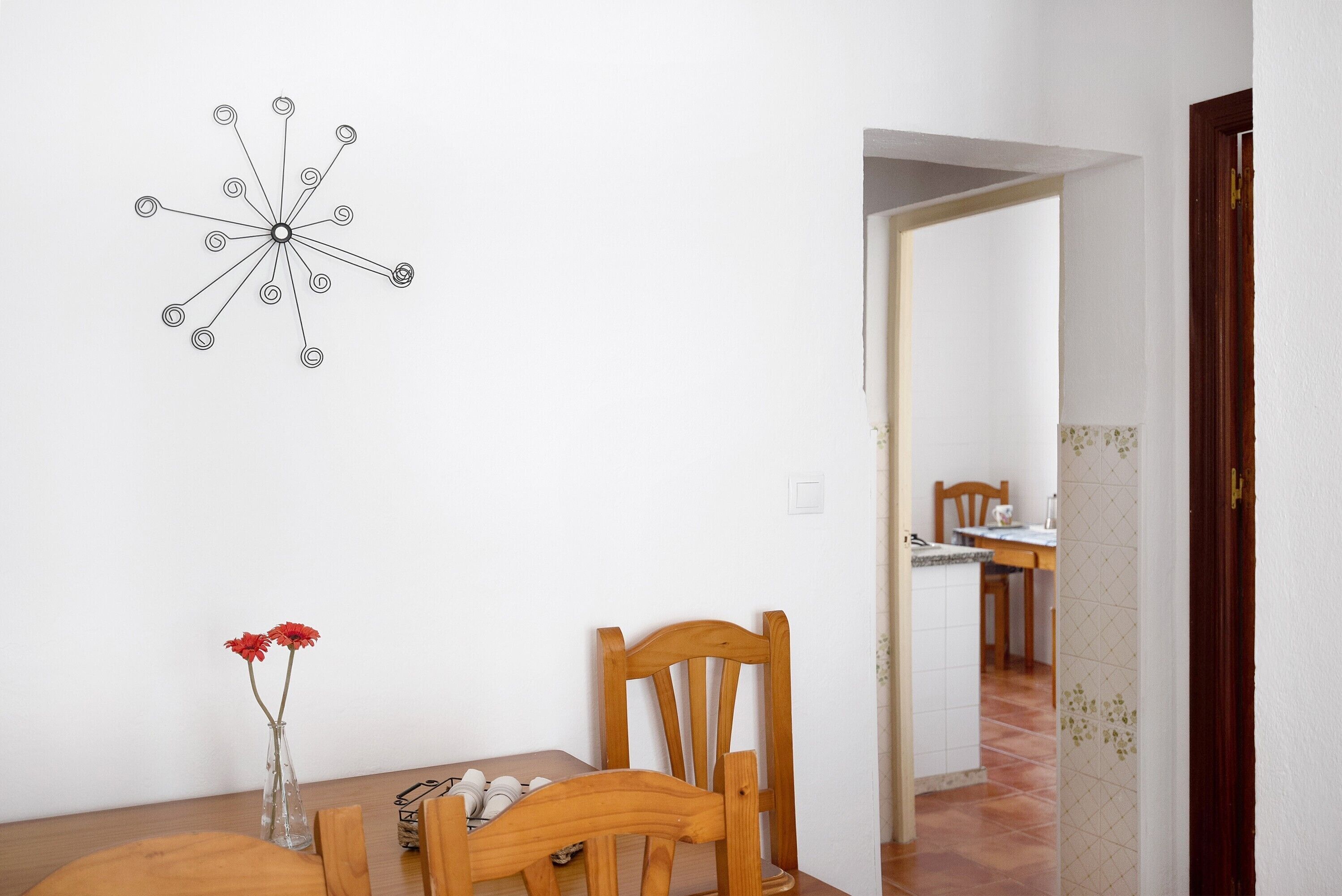 Un comedor con una mesa de madera, una silla, un florero con flores y una obra de arte en la pared.