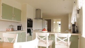 A kitchen with white cabinets, a microwave, an oven, and a refrigerator. There are two white chairs and a wooden table. - Lovely farm stay in the northern Granite Belt.  8 minutes from wineries. (Dalveen)