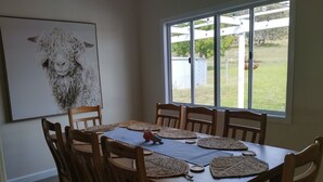 A dining area with a wooden table and chairs, a large window with a view of a yard, and a framed artwork on the wall. - Lovely farm stay in the northern Granite Belt.  8 minutes from wineries. (Dalveen)