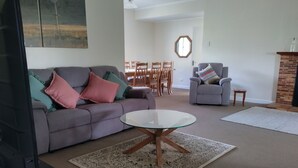 A living room with a grey sofa, a glass coffee table, a patterned rug, a dining area with wooden chairs, and a brick fireplace. - Lovely farm stay in the northern Granite Belt.  8 minutes from wineries. (Dalveen)