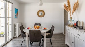 A dining area with a round table, four chairs, a white ceiling light, a decorative mirror, and a view of the outdoors through large windows.