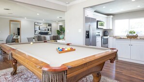 Un tavolo da biliardo in un soggiorno moderno, con una cucina sullo sfondo.