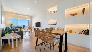 Ein modernes Wohnzimmer mit Essbereich, einer Couch, einem Fernseher und einem Balkon mit Blick.