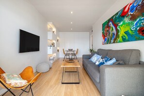 A modern living room with a flat-screen TV, a grey sofa, a wooden coffee table, and a colorful abstract painting.